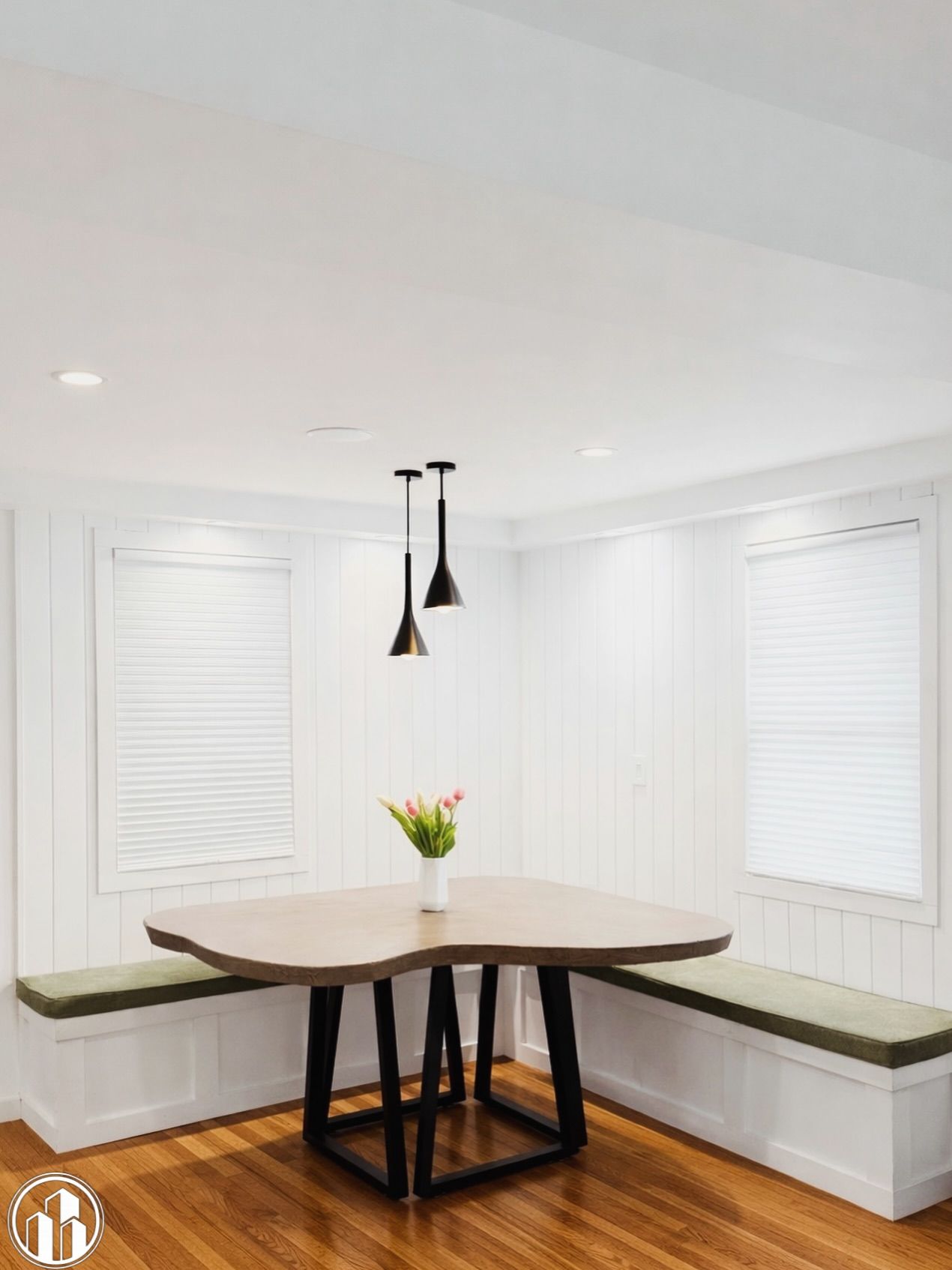 Bright breakfast nook with built-in bench, round table, black pendant lights, and white blinds