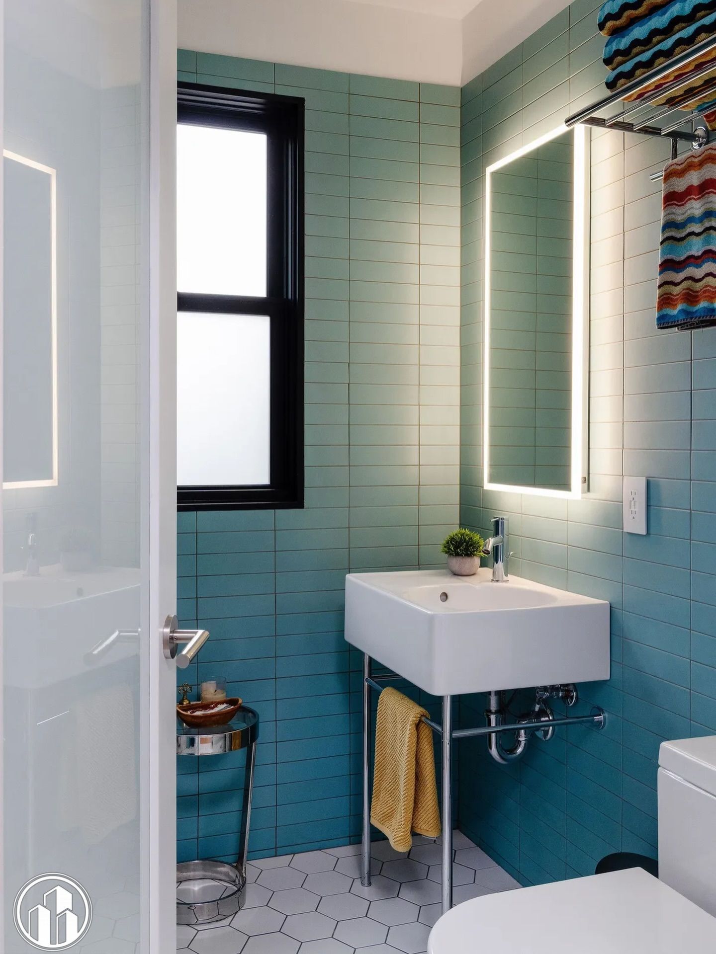 Bright mint-tile bathroom with a sink, mirror, window, and colorful shower curtain.