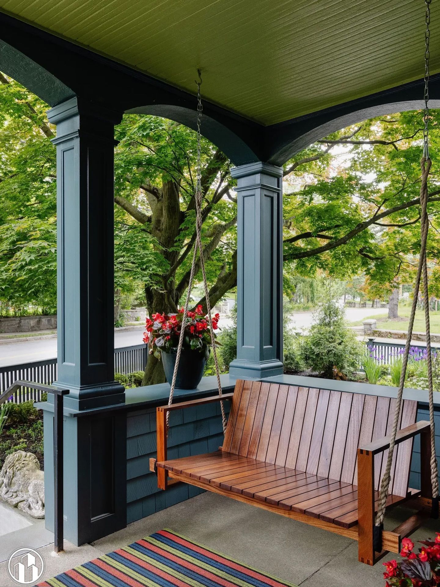 Covered porch with wooden bench, potted flowers, and green trees beyond the railing.