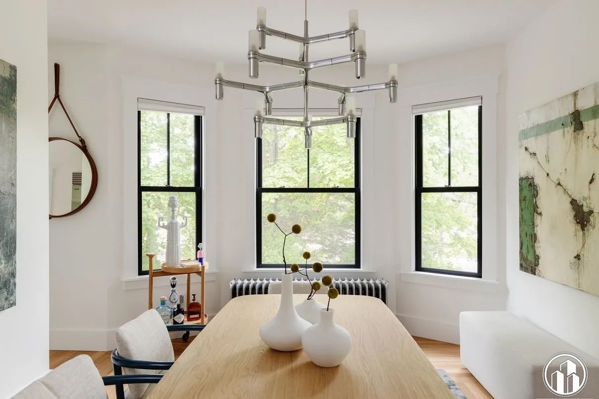 Bright dining room with a wooden table, white chairs, black-framed windows, and a modern chandelier.