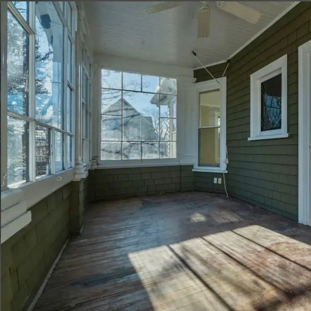 Empty screened porch with weathered wood floor, green siding, and large windows overlooking a snowy yard