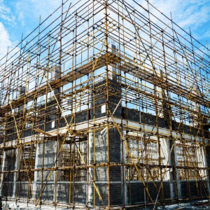 Scaffolding surrounds a multi-story building under construction against a blue sky.