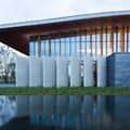Modern building with wooden slats, white columns, and a reflecting pool at dusk