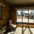 Unfinished brick room with sliding glass doors opening to a sunny balcony and city view.