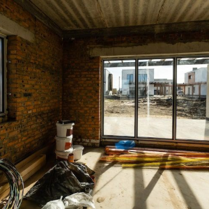 Unfinished brick room with sliding glass doors opening to a sunny balcony and city view.