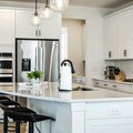 Bright white modern kitchen with island, bar stools, stainless appliances, and pendant lights