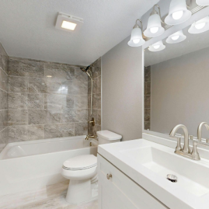Bright bathroom with white vanity, mirror lights, tiled shower, and bathtub