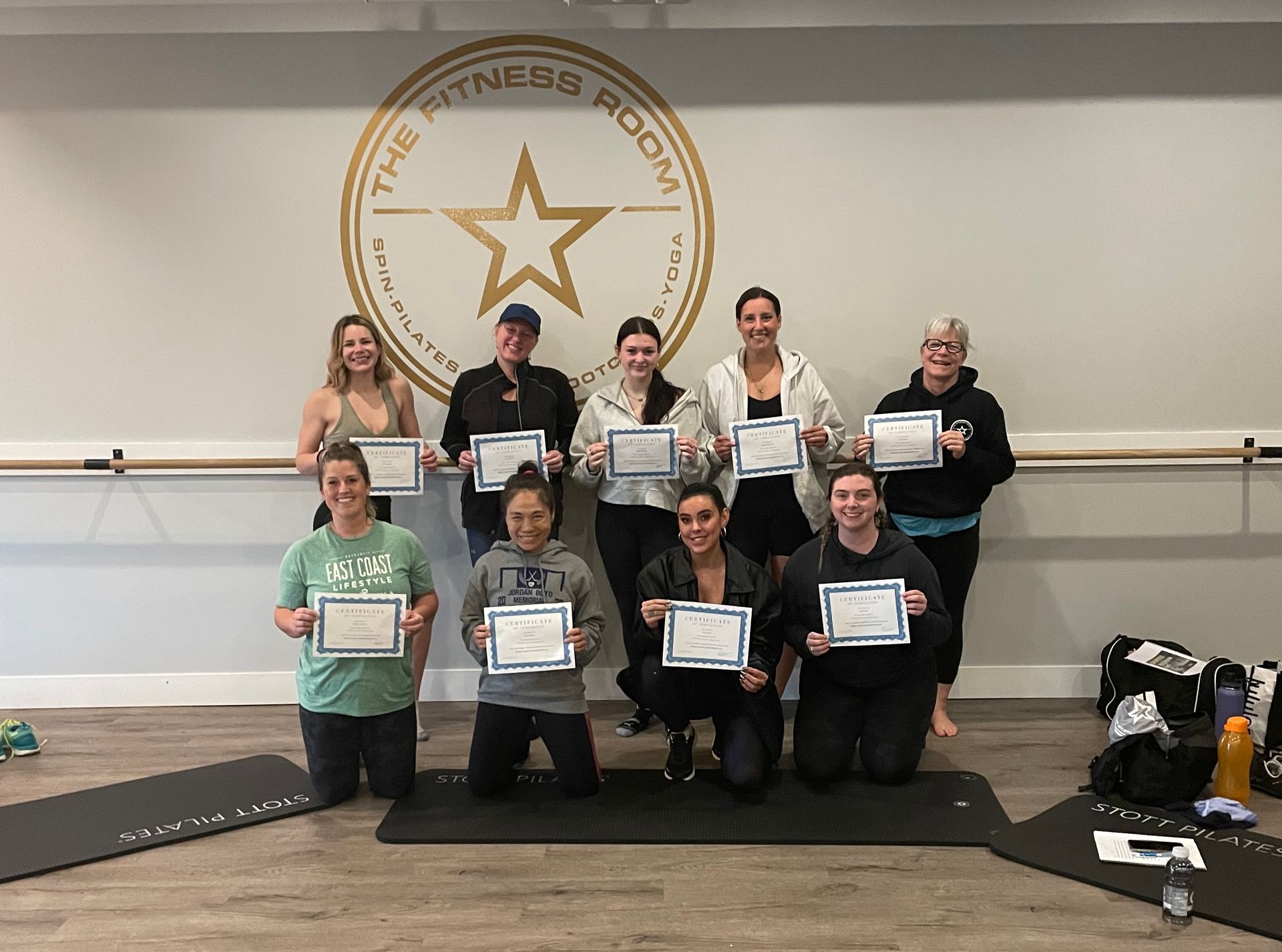 Group of people kneeling and standing with certificates in a dance studio, posed before a star wall logo.