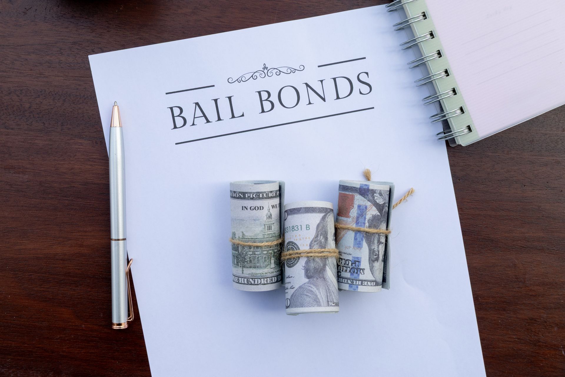 Bail Bonds document with rolled cash, a pen and spiral notebook on a wooden desk