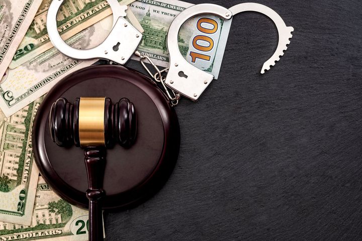 A gavel and handcuffs on top of some cash.