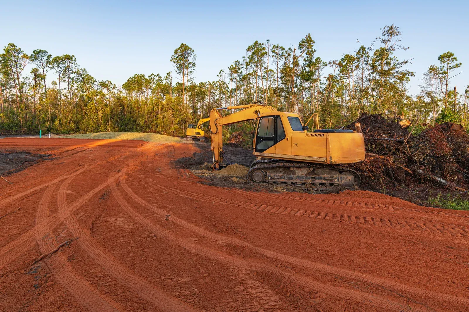 Yellow bulldozer pushing dirt in a muddy clearing beside a dense green forest
