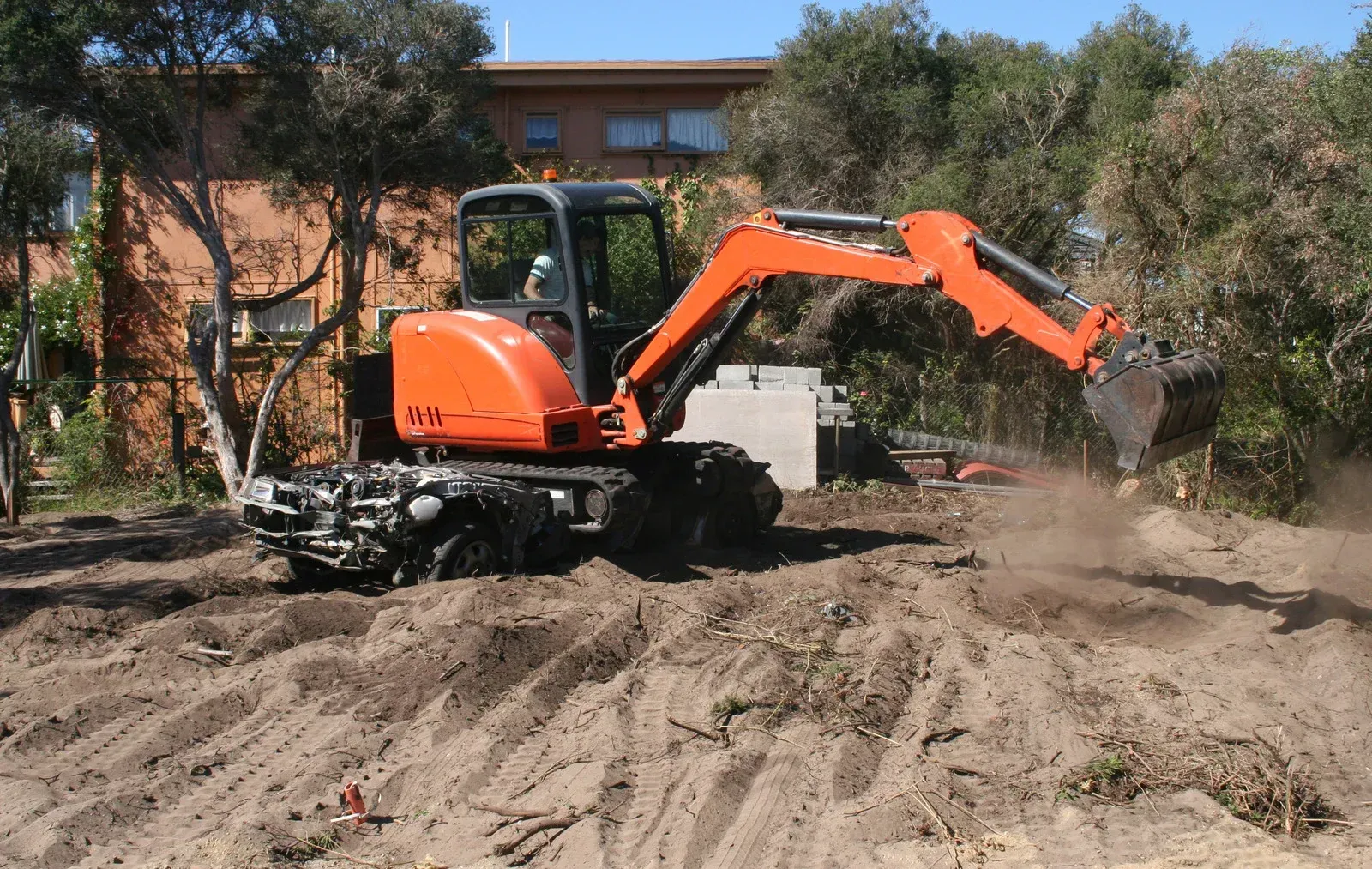 Excavator digging soil in a wooded area with autumn trees