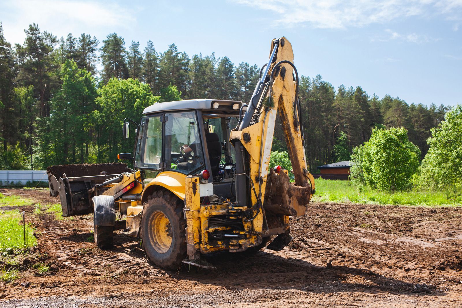 Yellow excavator clearing a wooded area, moving logs and debris in a forest clearing