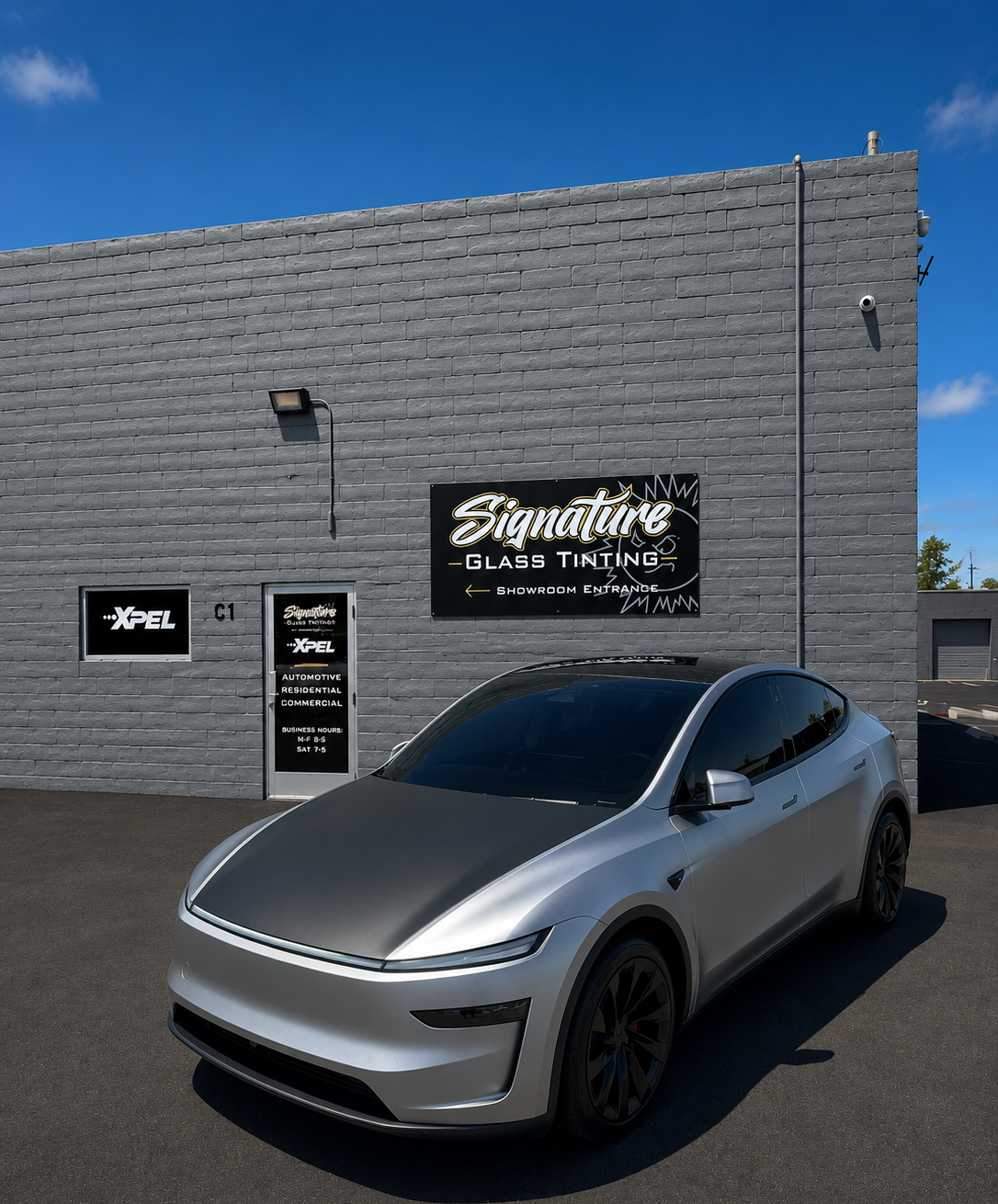 Silver Tesla parked outside a black brick storefront with a “Signature” sign