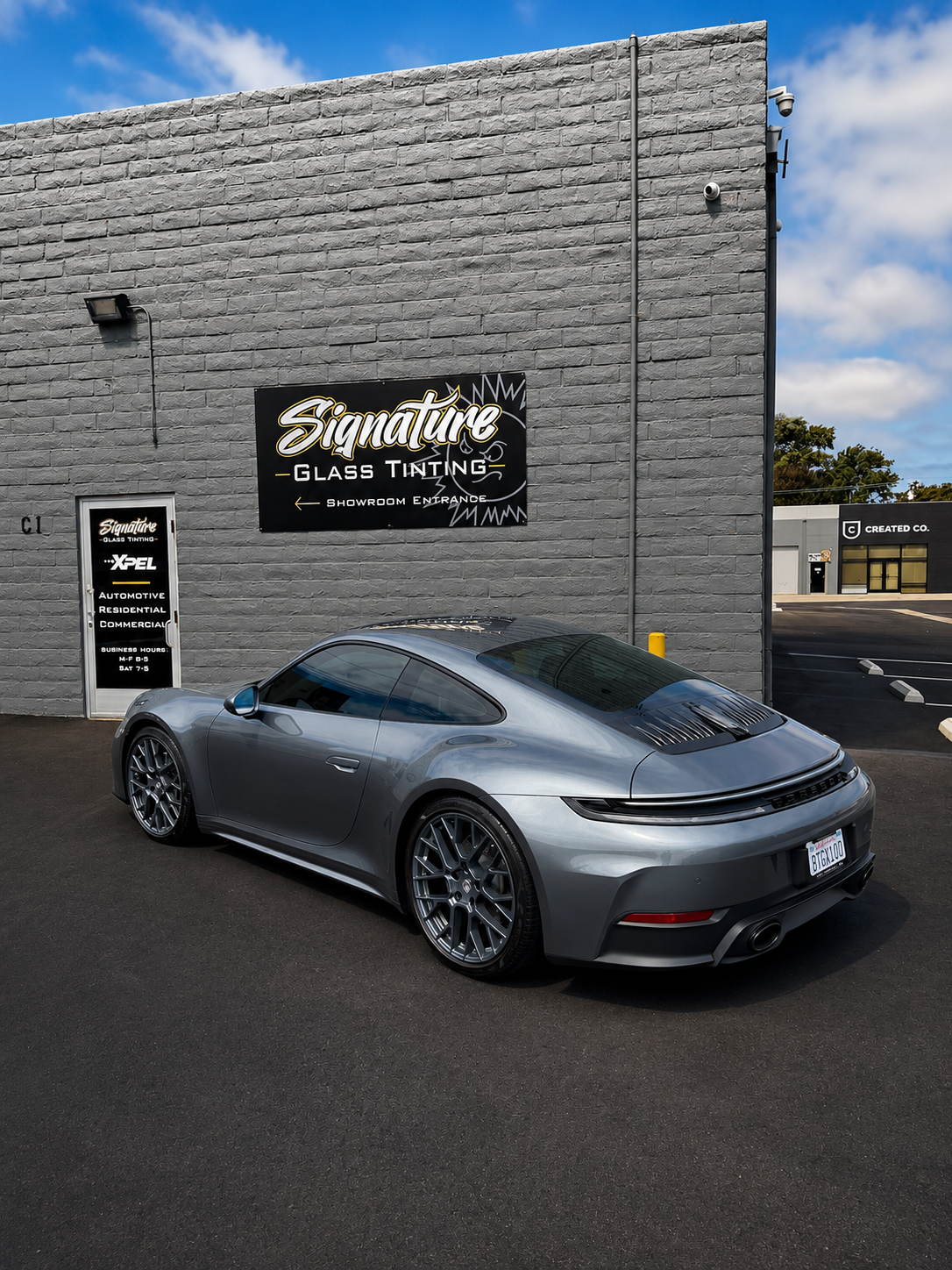 Gray sports car parked outside Signature’s Garage & Tire shop on a brick building.