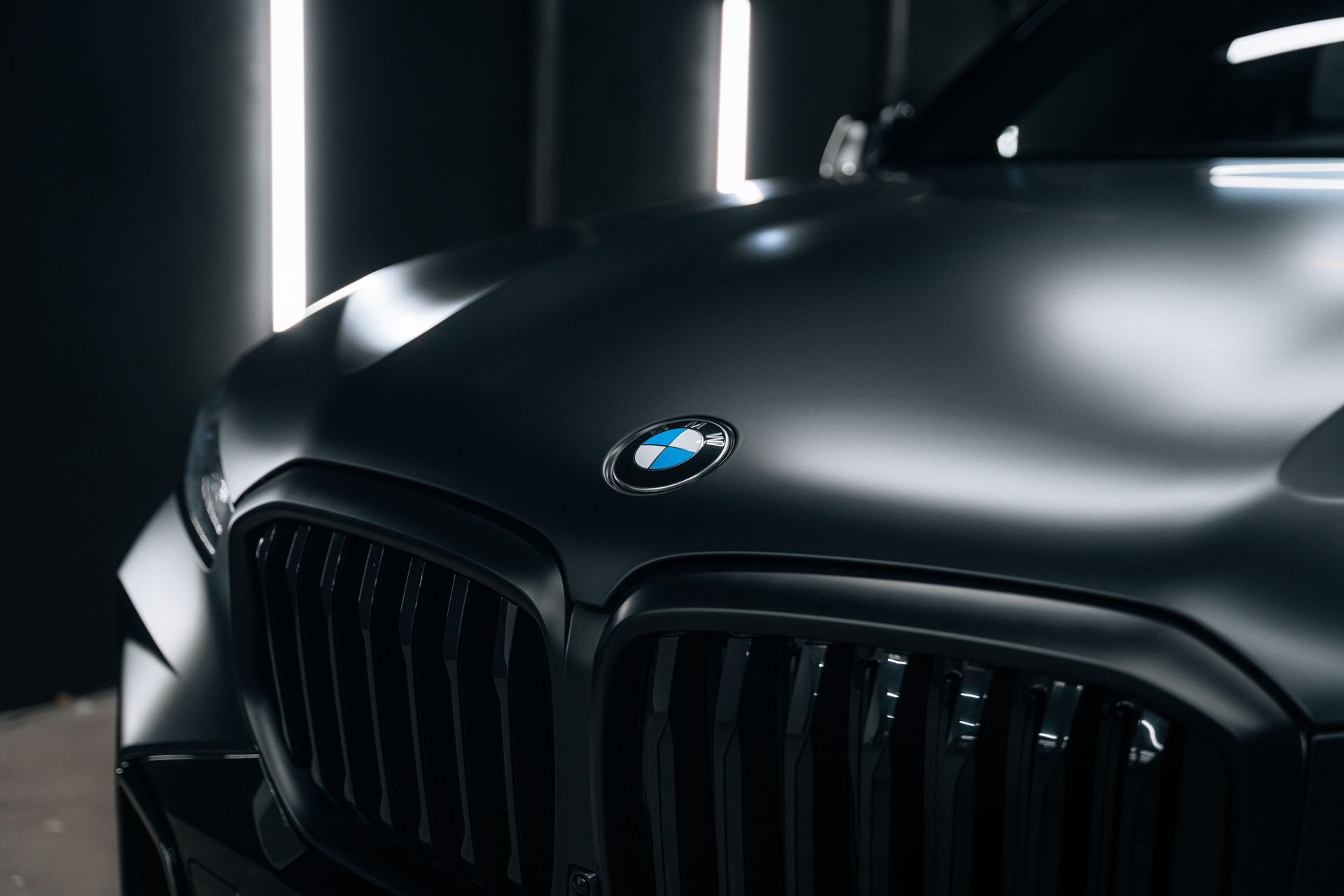 Close-up of a black BMW front grille and hood in a dark studio with vertical lights