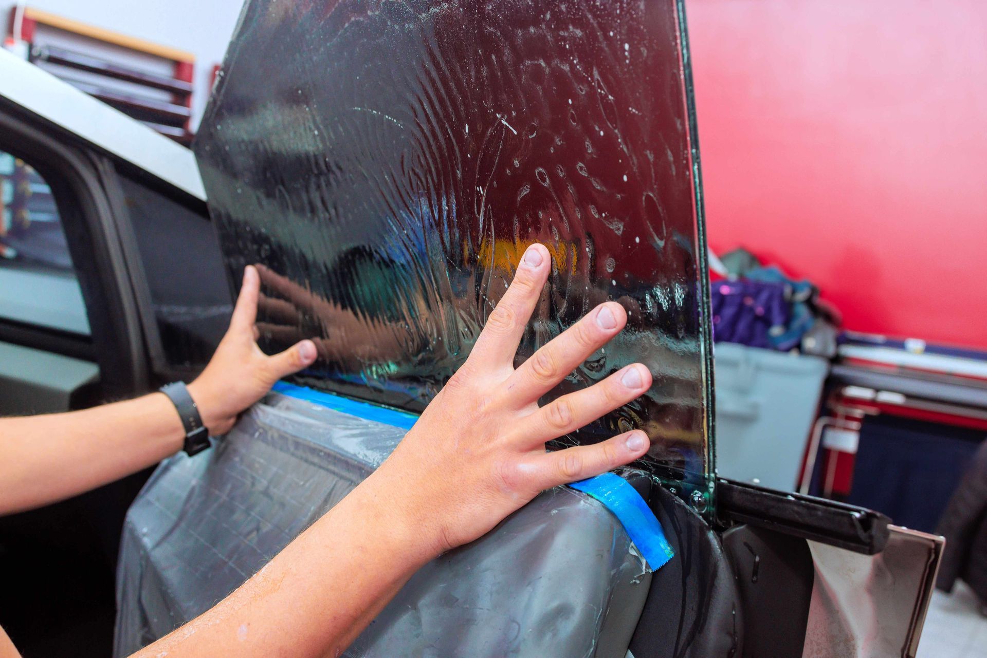 Hands installing tinted glass on a car door in a workshop