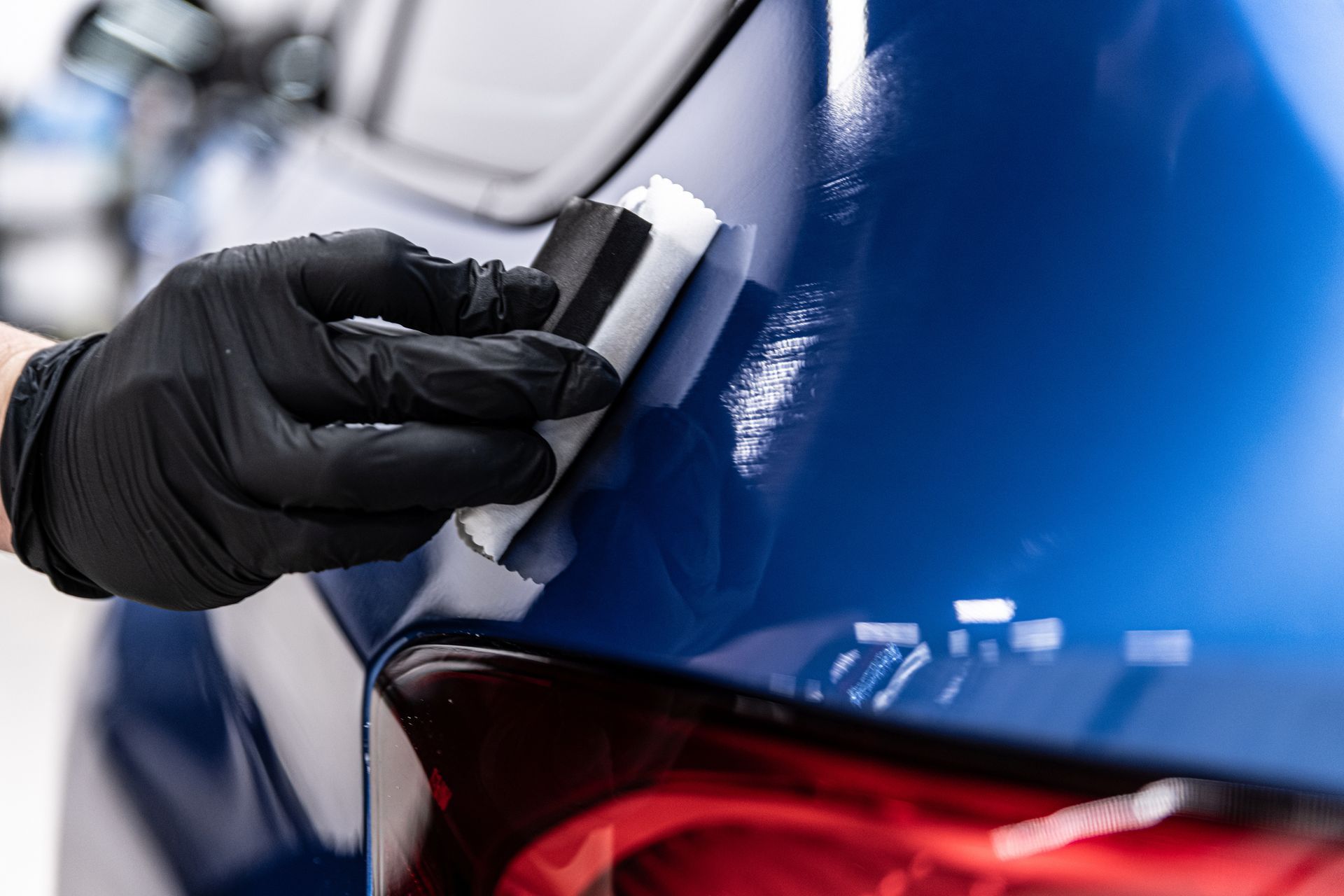 Gloved hand polishing a blue car near the rear taillight