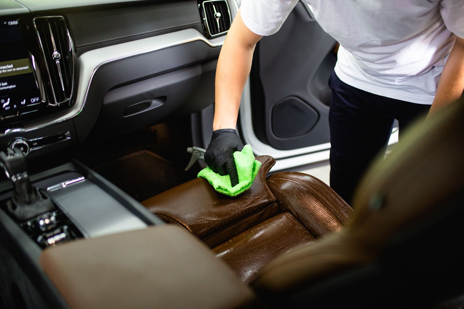 A gloved technician cleaning a leather car seat and console with a microfiber cloth. A gloved technician cleaning a leather car seat and console with a microfiber cloth.
