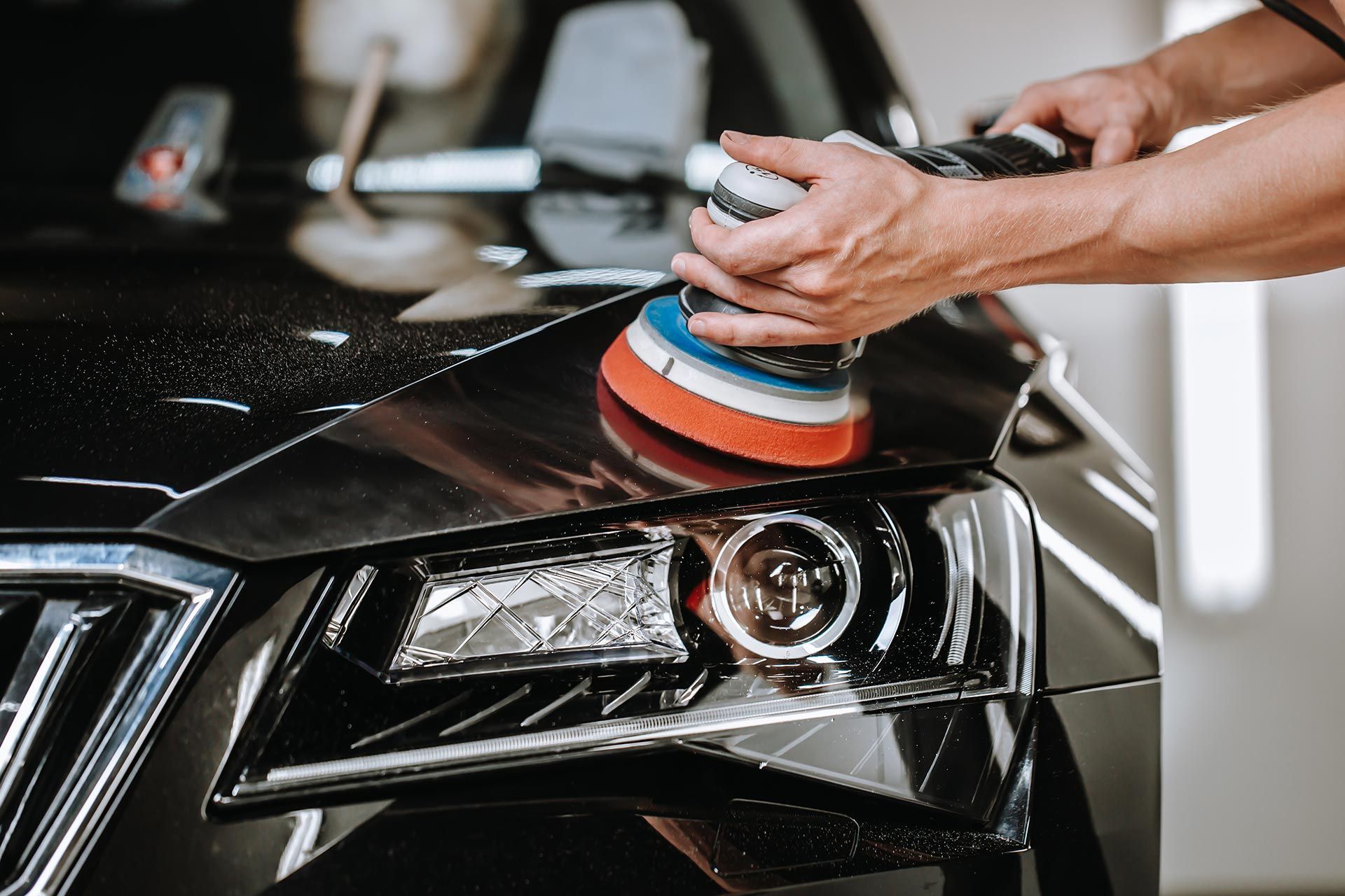 Person polishing a car hood with an electric buffer near a headlight. Person polishing a car hood with an electric buffer near a headlight.