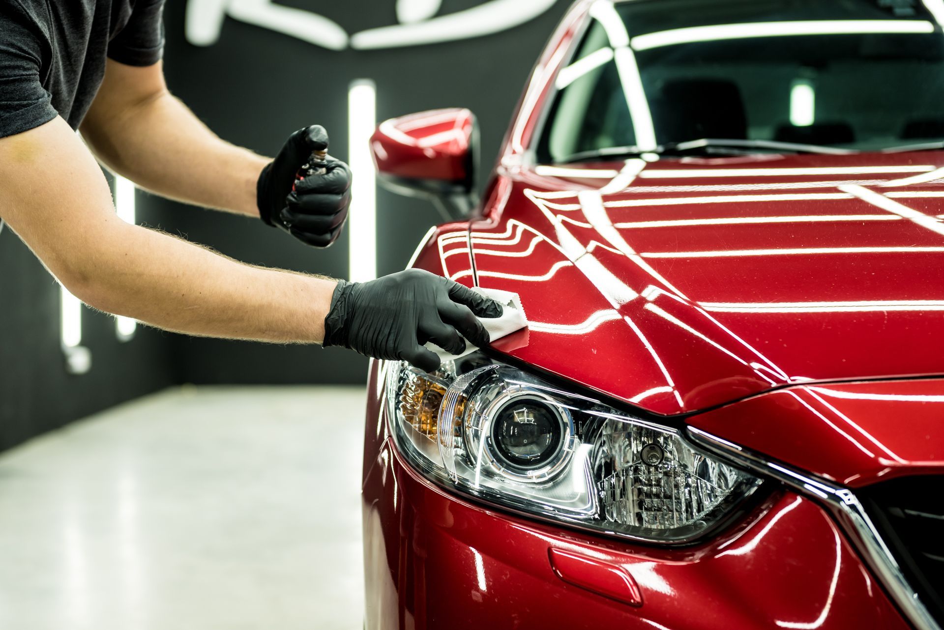Detailing a red sports car’s front headlight and hood with a technician in black gloves polishing it