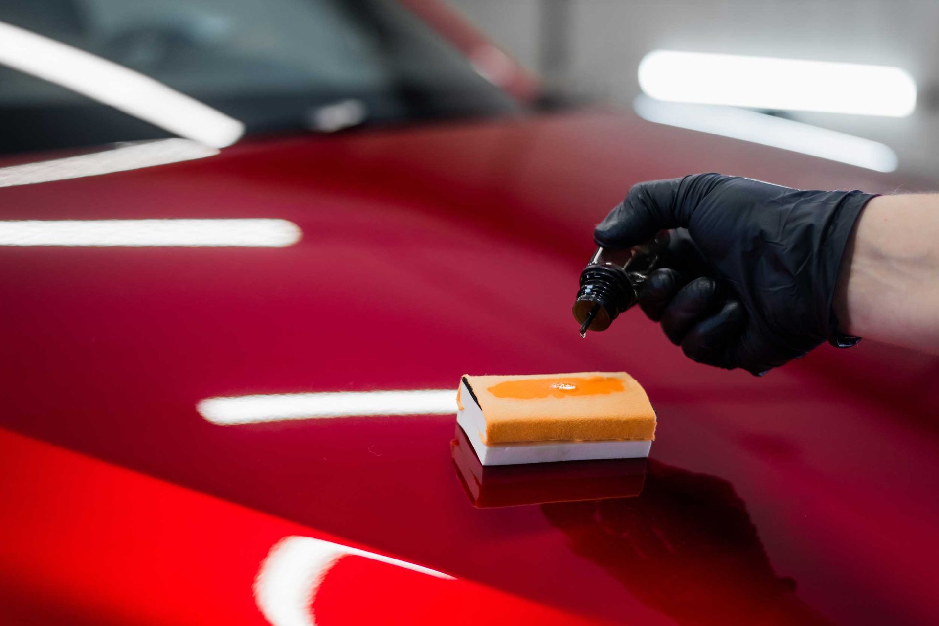 Gloved hand polishing a glossy red car with a sponge applicator