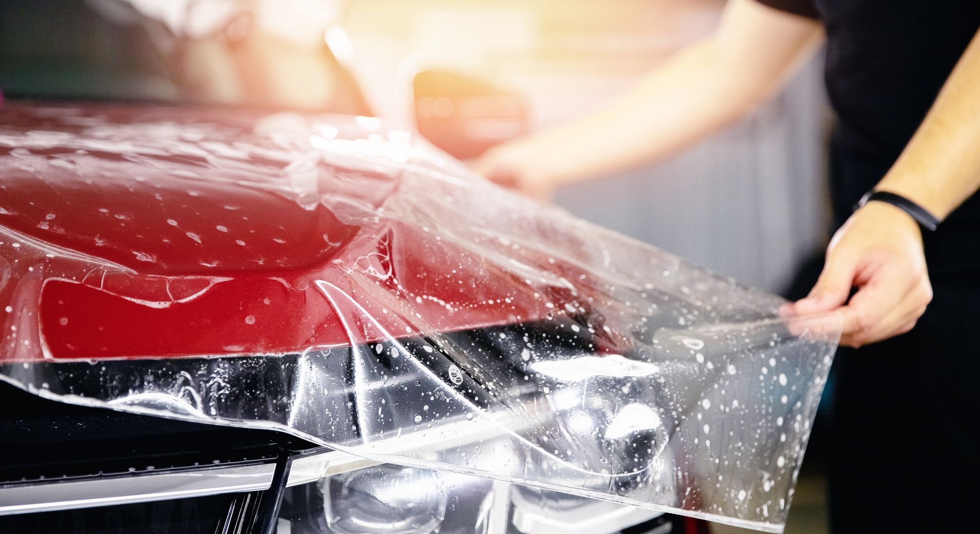 Person applying a clear protective film to the hood of a red car Person applying transparent protective film to a red car hood in a garage