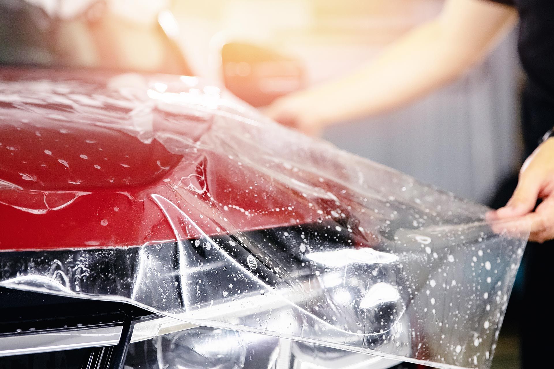 Applying clear paint protection film to a red vehicle headlight and hood. Applying clear paint protection film to a red vehicle headlight and hood.