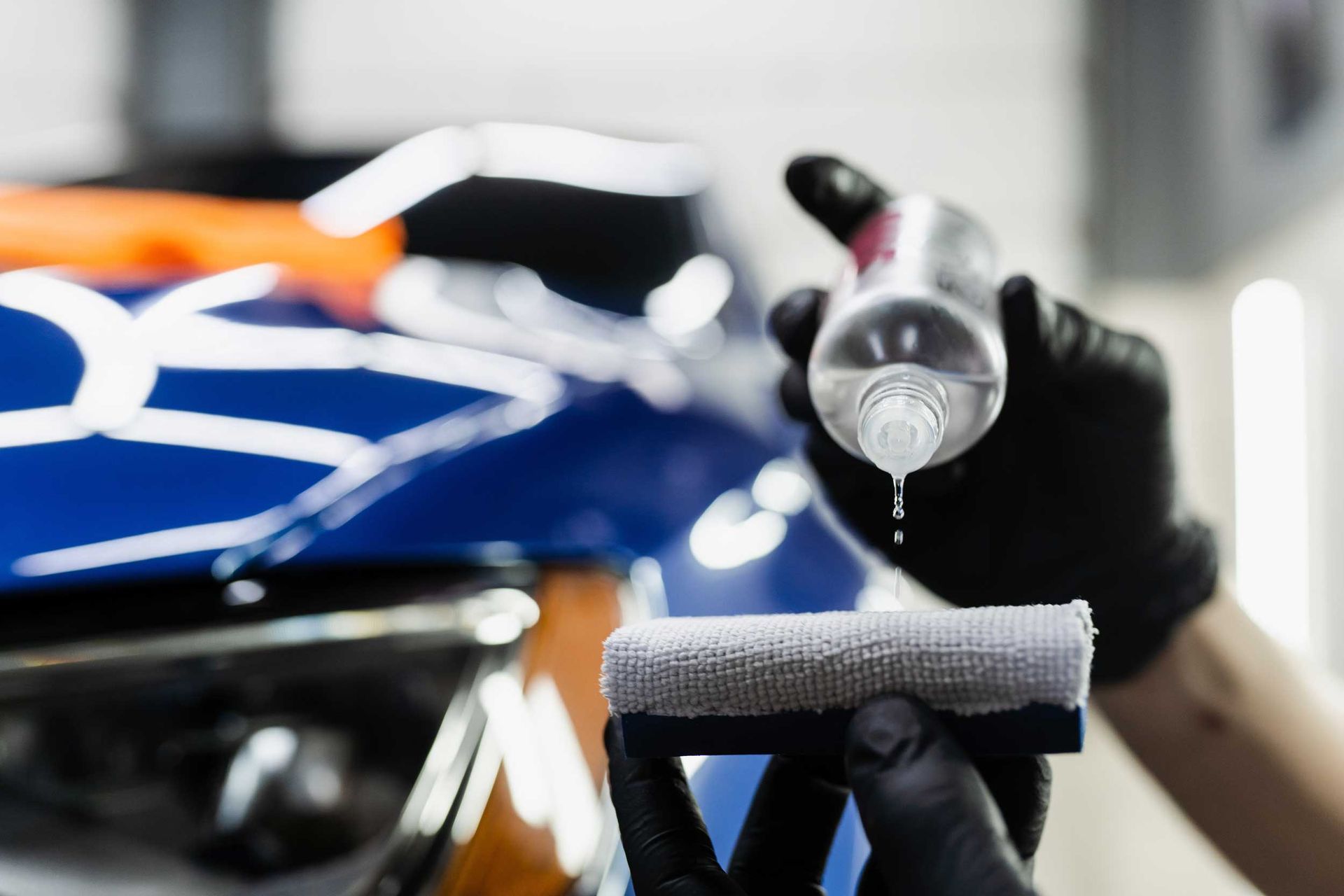 Gloved hand applying polish to a blue car’s headlight with a microfiber pad