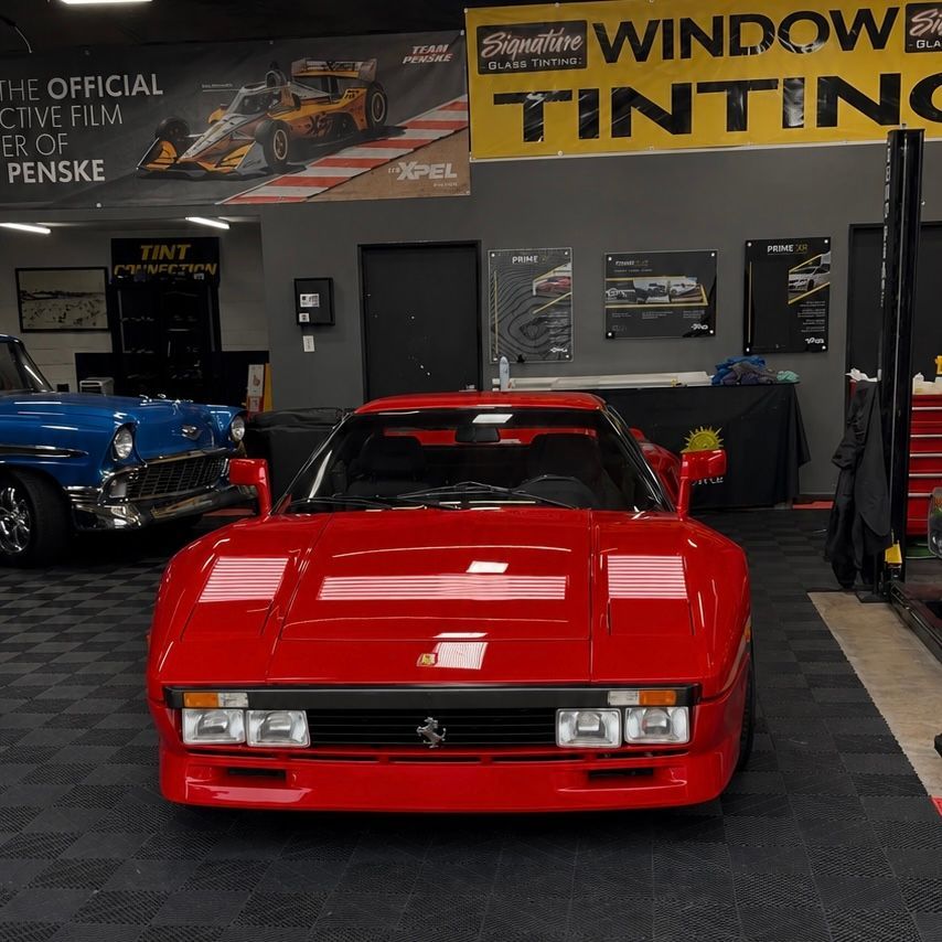Red sports car in a garage, with window tinting signs and a blue car in the background.