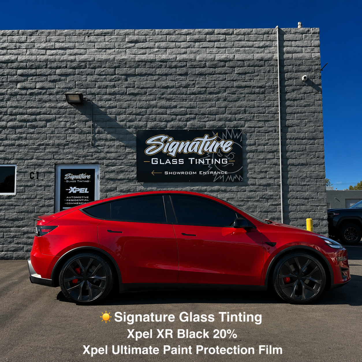 Red Tesla parked by Signature Glass Tinting building with text advertising XPEL XR Black 20% window film