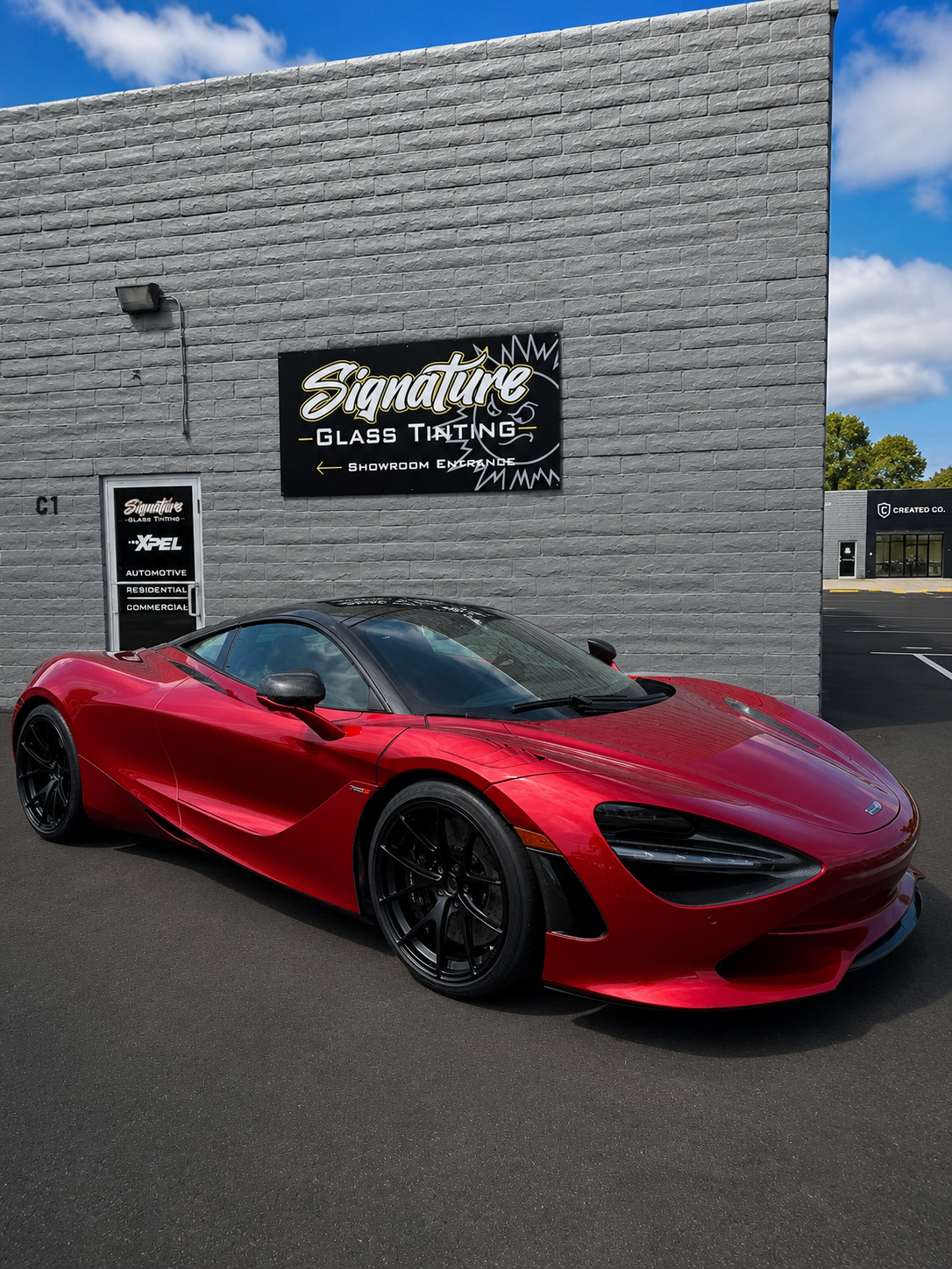 Red sports car parked outside a gray building with a sign above the entrance.