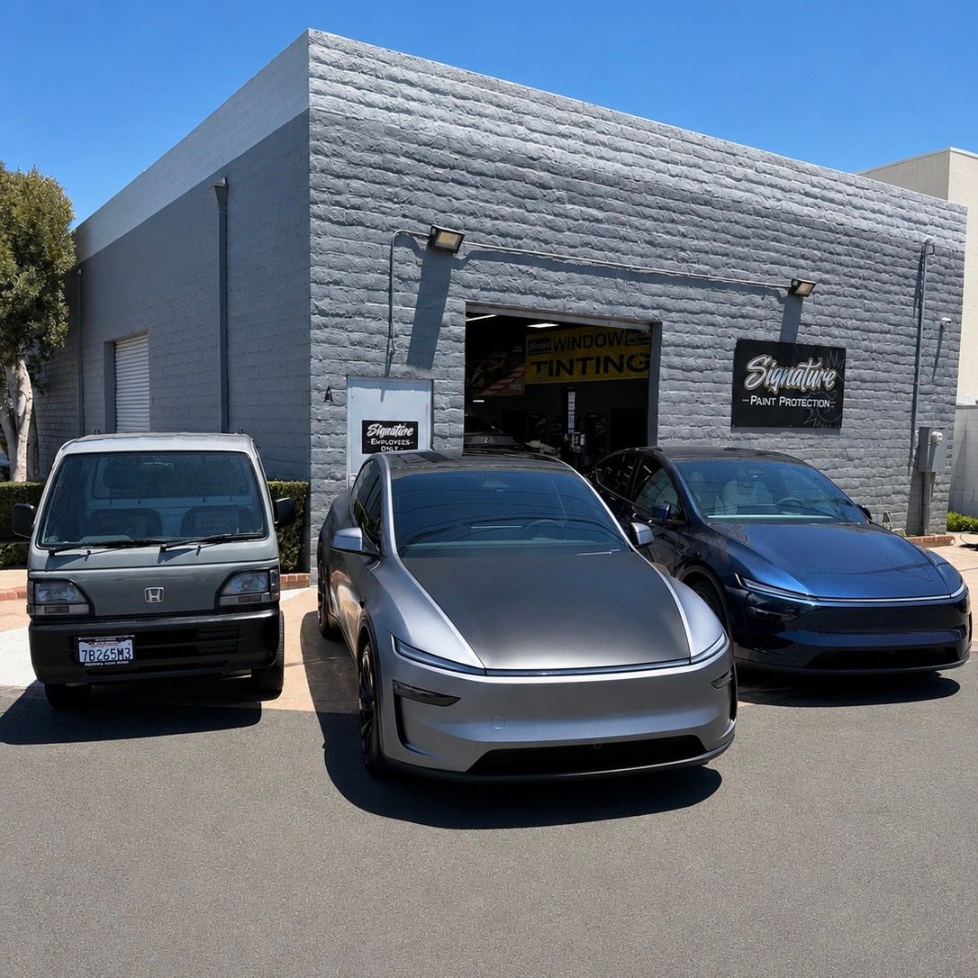 Three parked cars outside a gray auto shop on a sunny street.