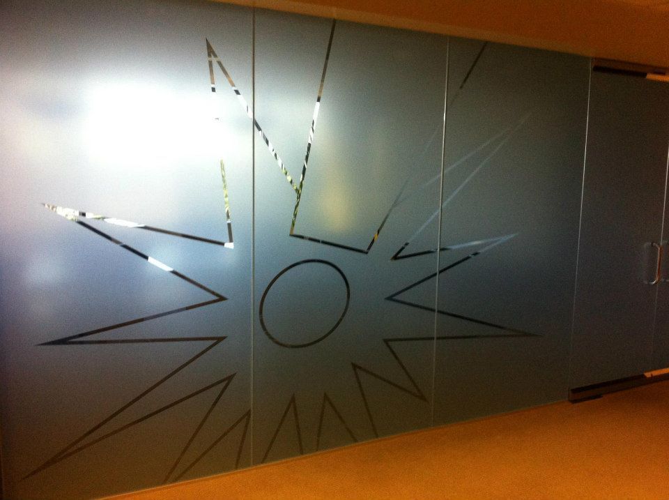 Frosted glass wall with a black sunburst graphic and circular center, lit by warm indoor light