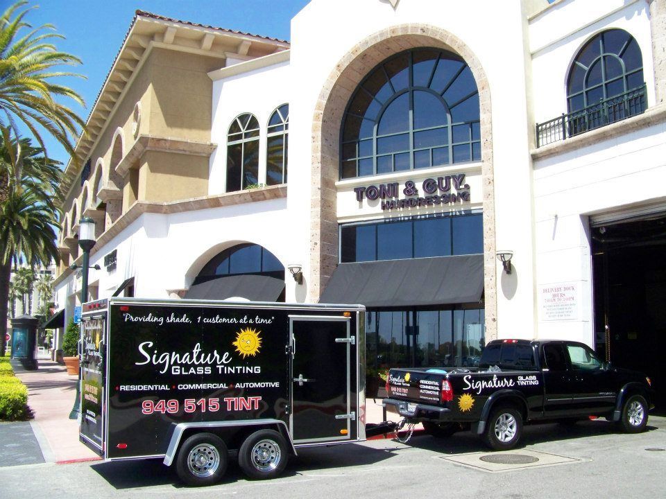 Black delivery truck and trailer parked outside a white building with arched windows and a palm tree.