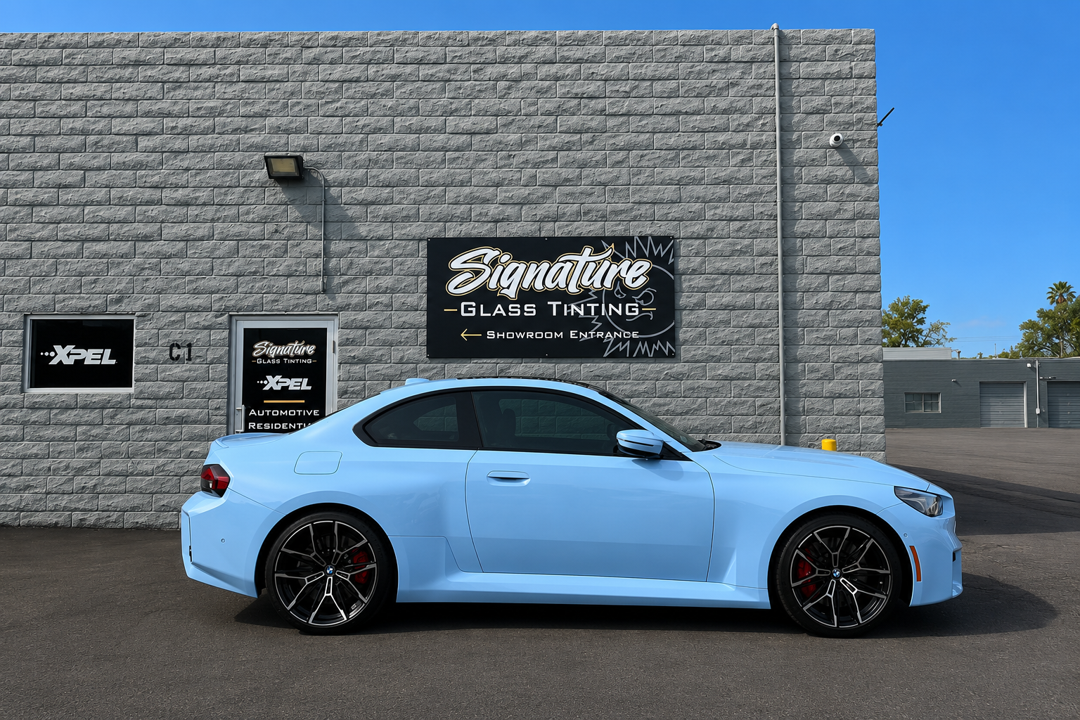 Ferrari Purosangue At Tint Shop. Light blue sports sedan parked beside a gray cinderblock wall with shop signs under a clear sky