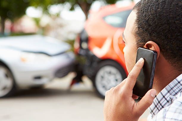 Accident victim standing in front of two damaged cars, holding a phone and calling for help