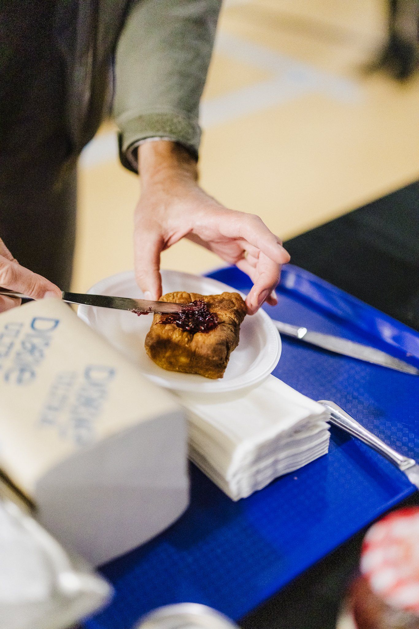 Person cutting a piece of food on a small white plate with a knife. Blue cutting board and paper towels visible.
