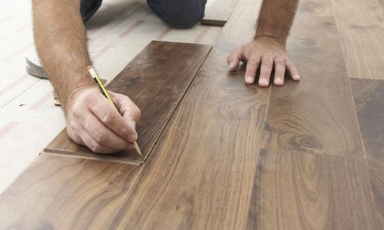 Man using a pencil to mark flooring he planks he is installing on the floor