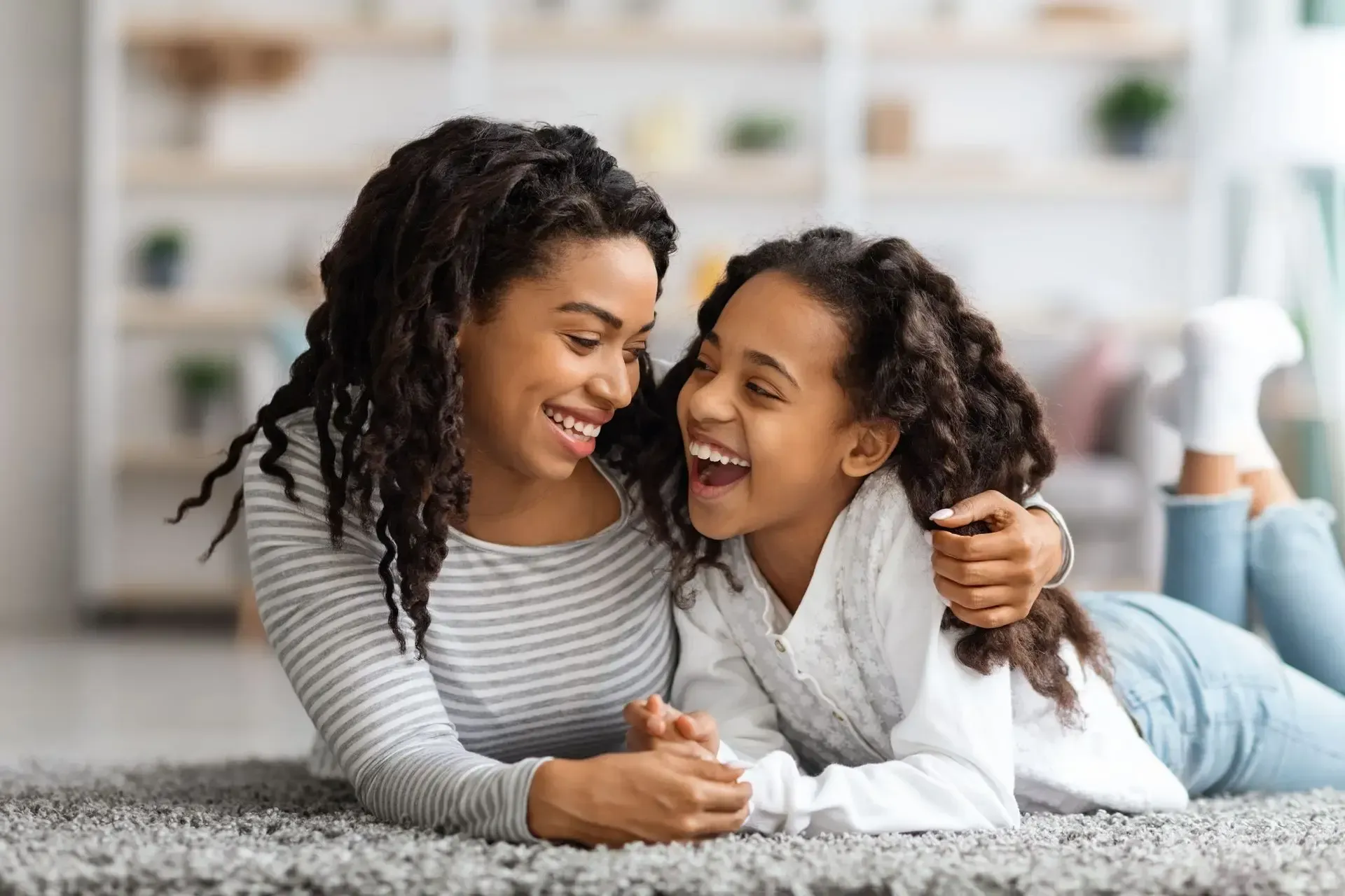 A mother and daughter laughing together on a carpet