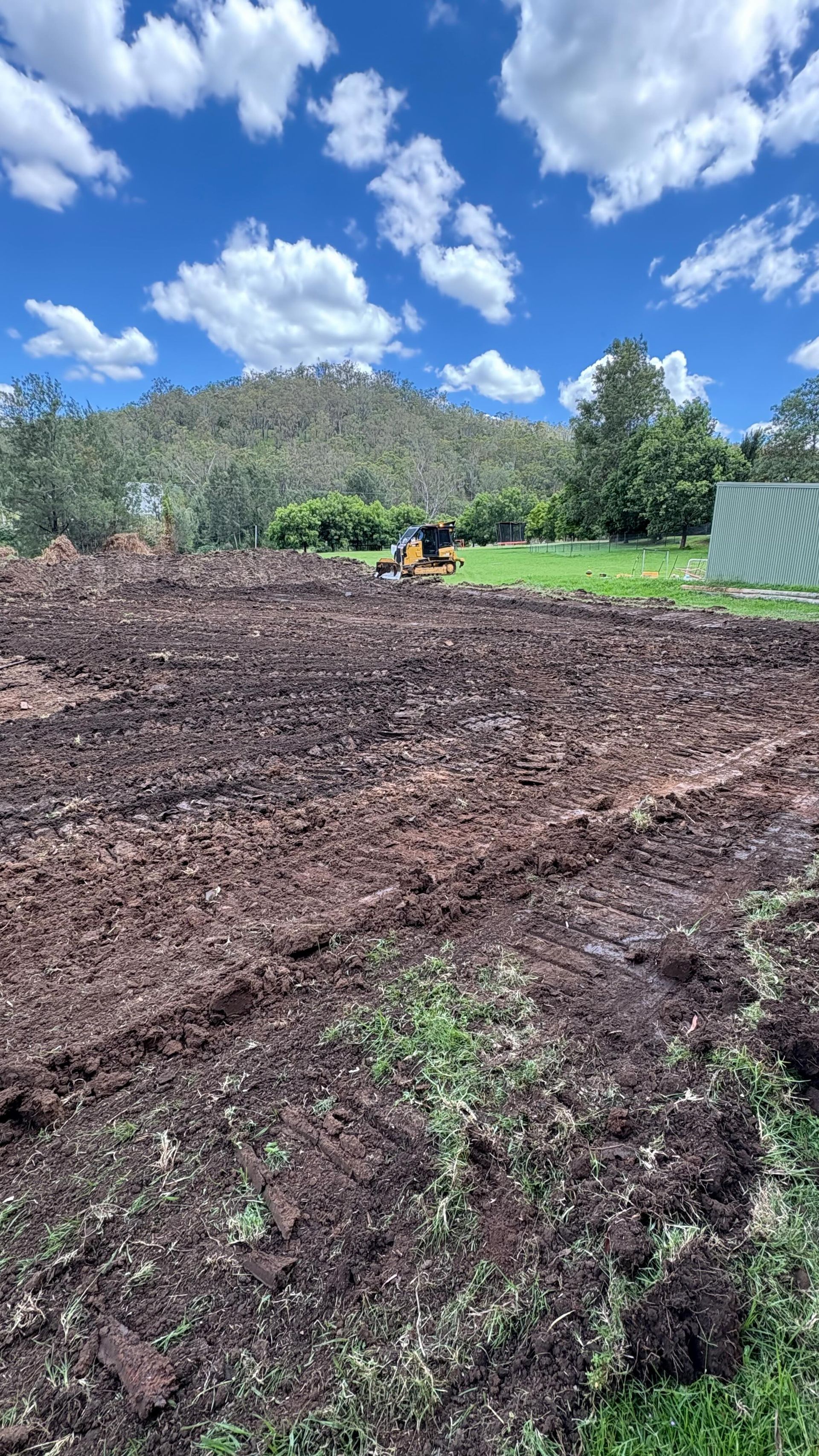Freshly tilled brown field with green trees, hills, and a blue sky with clouds