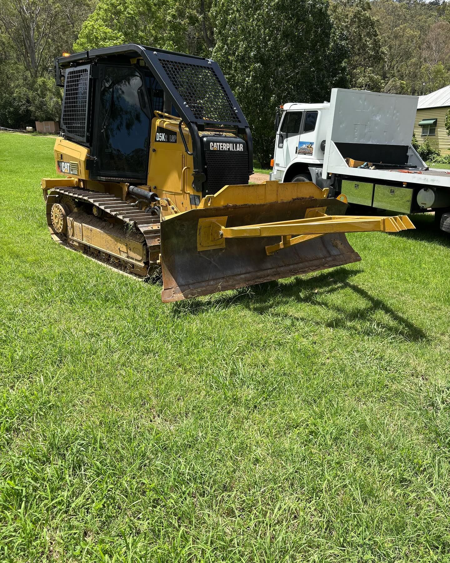 Yellow tracked skid steer with front blade parked on grass outdoors