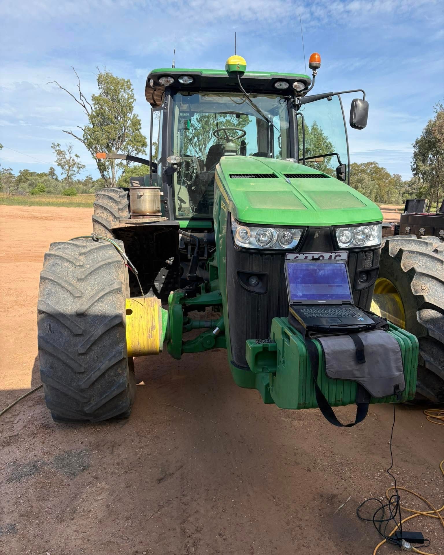 Green tractor on a dirt road, front-facing with large tires and a front-mounted attachment.