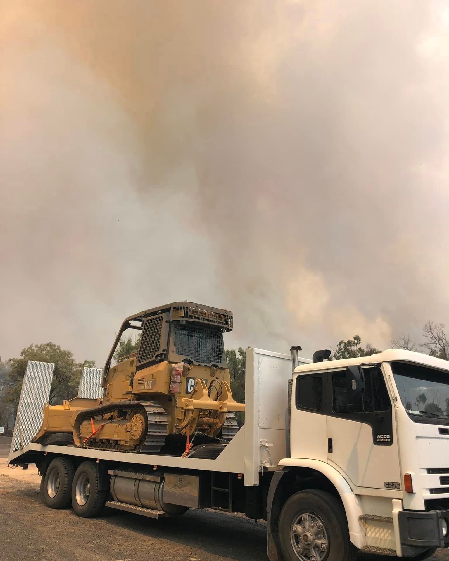 White flatbed truck carrying a bulldozer on a smoky road