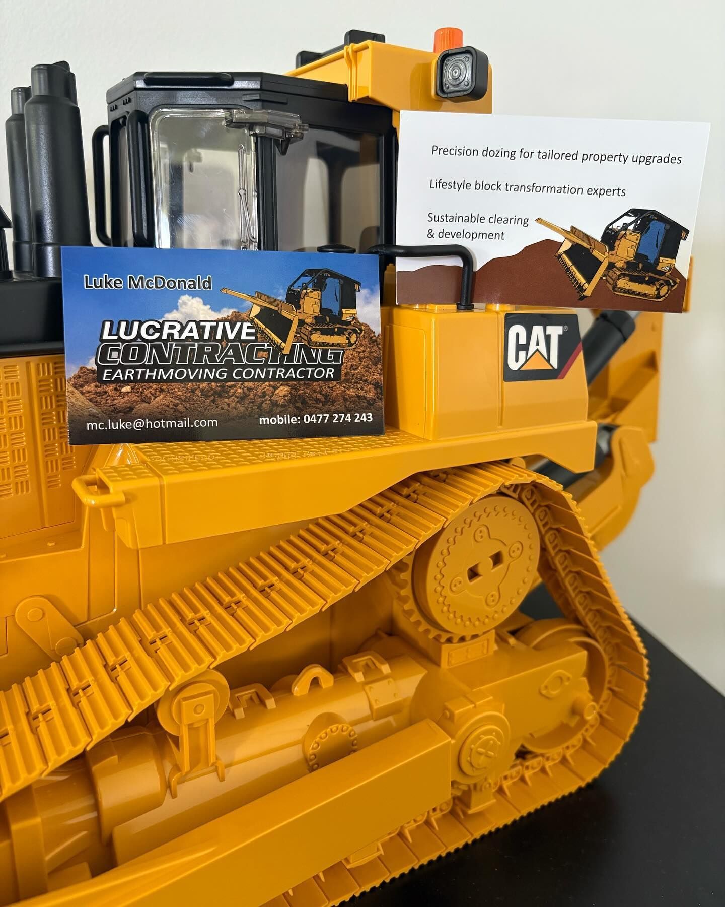 Yellow CAT bulldozer model with a “LURCATIVE” card on it against a white background