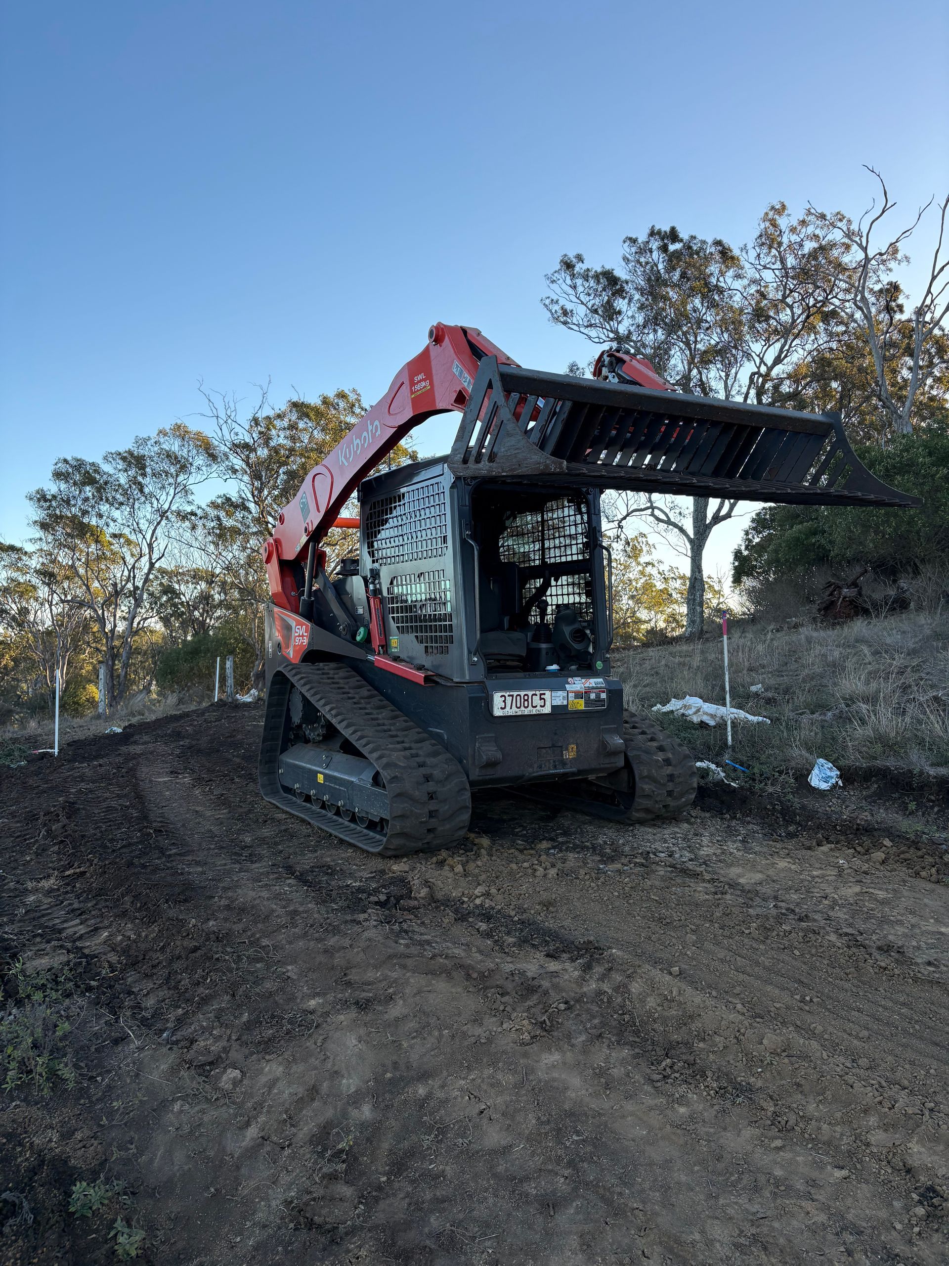 Excavator on a dirt mound at sunset under a dramatic orange sky