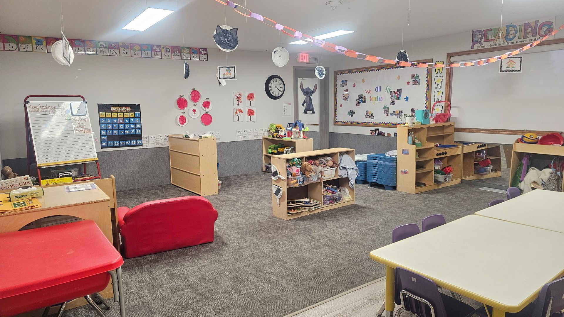 Classroom with tables, shelves, a red couch, and decorations; ready for children.