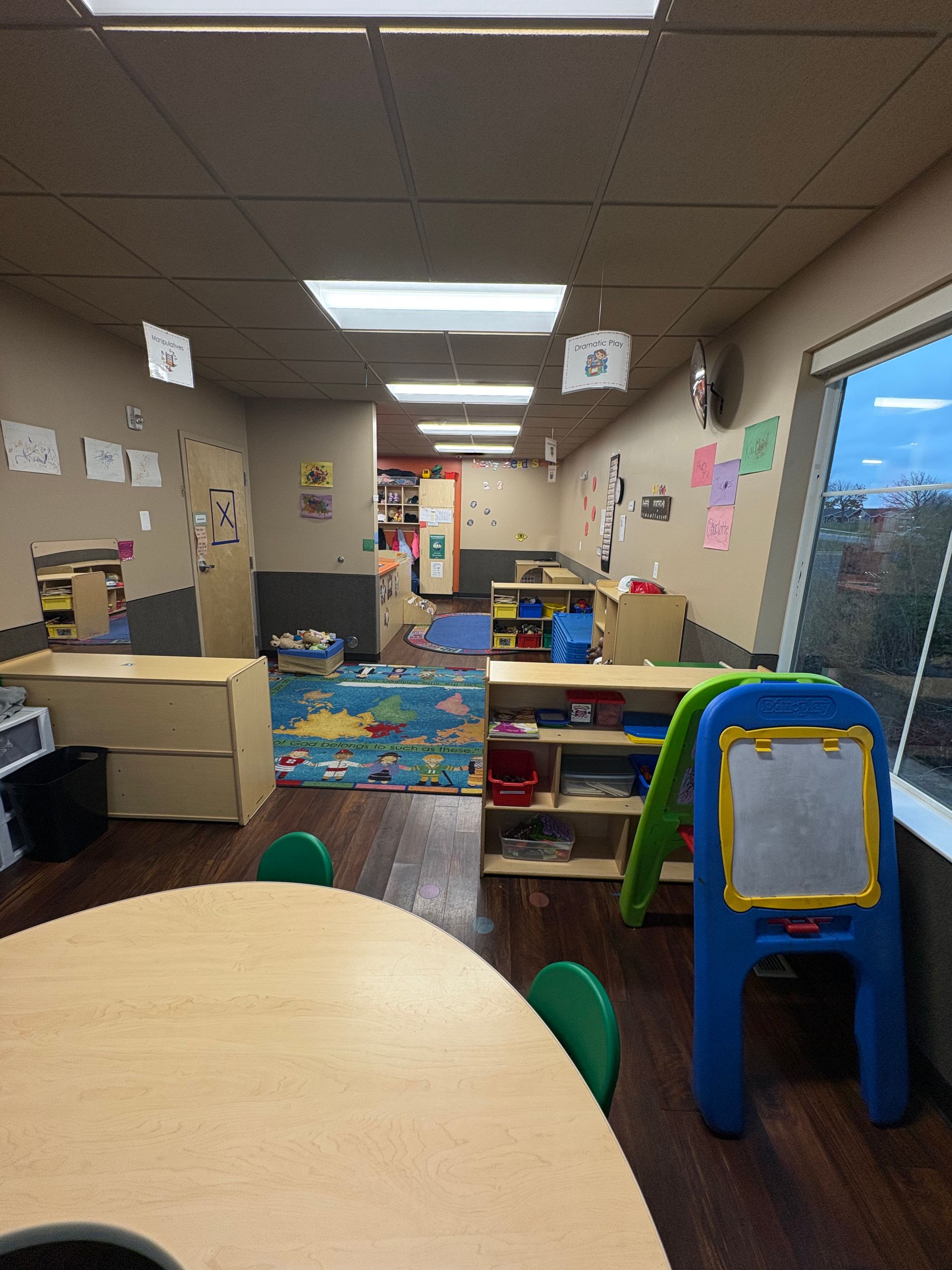 Childcare classroom with round table, shelving, a window, and play equipment.