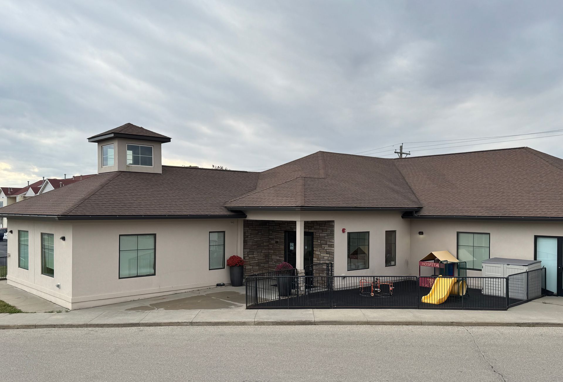 Tan building with brown patterned roof and small playground.