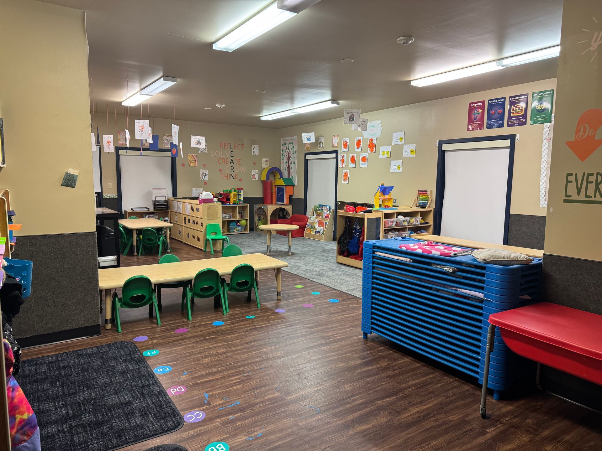 A colorful preschool classroom with tables, chairs, toys, and learning materials.